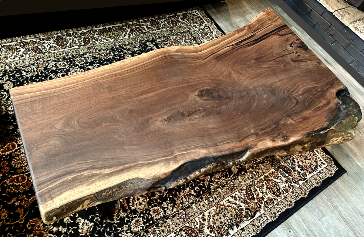 Top-down view of large live edge black walnut coffee table, highlighting natural wood grain, and live edge details. Handcrafted live edge walnut coffee table styled in a modern living room with a cozy, rustic aesthetic. Detailed view of live edge walnut wood grain, showing natural color variations, and organic patterns. Large live edge black walnut coffee table made from walnut featuring unique grain patterns and a smooth, polished surface. Rustic and modern design.