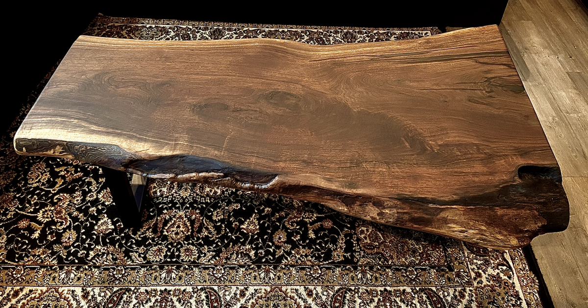 Top-down view of large live edge black walnut coffee table, highlighting natural wood grain, and live edge details. Handcrafted live edge walnut coffee table styled in a modern living room with a cozy, rustic aesthetic. Detailed view of live edge walnut wood grain, showing natural color variations, and organic patterns. Large live edge black walnut coffee table made from walnut featuring unique grain patterns and a smooth, polished surface. Rustic and modern design.