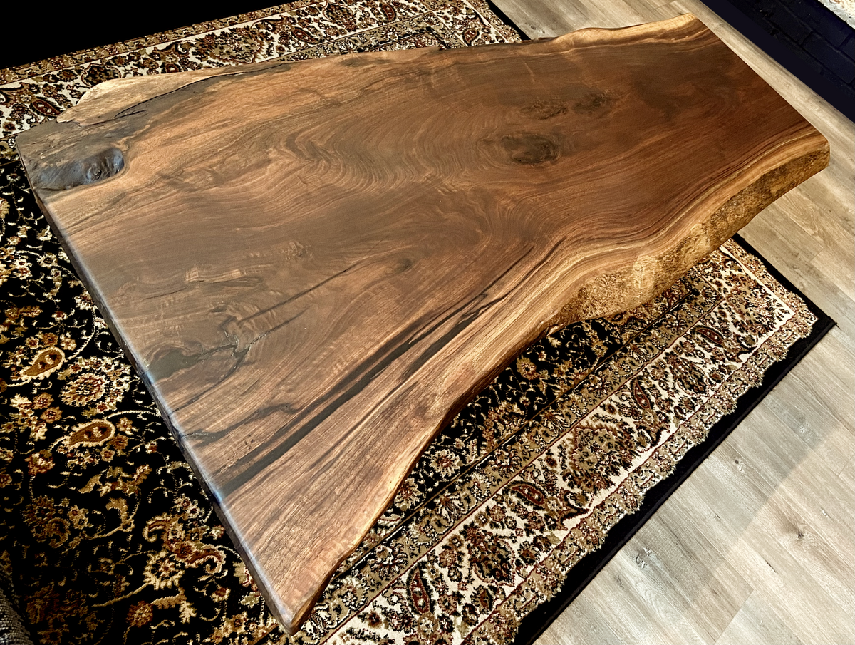 Top-down view of large live edge black walnut coffee table, highlighting natural wood grain, and live edge details. Handcrafted live edge walnut coffee table styled in a modern living room with a cozy, rustic aesthetic. Detailed view of live edge walnut wood grain, showing natural color variations, and organic patterns. Large live edge black walnut coffee table made from walnut featuring unique grain patterns and a smooth, polished surface. Rustic and modern design.