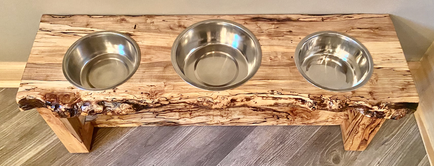 Live edge raised pet stand crafted from spalted maple or black walnut, featuring two stainless steel bowls for food and water. Elevated pet feeder, showcasing the natural wood grain and sturdy construction. Top-down view highlighting the placement of the three stainless steel bowls within the live edge wooden stand. Detailed close-up of the spalted maple’s unique wood grain patterns on the pet stand.