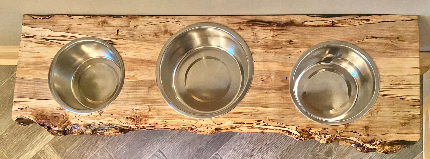 Live edge raised pet stand crafted from spalted maple or black walnut, featuring two stainless steel bowls for food and water. Elevated pet feeder, showcasing the natural wood grain and sturdy construction. Top-down view highlighting the placement of the three stainless steel bowls within the live edge wooden stand. Detailed close-up of the spalted maple’s unique wood grain patterns on the pet stand.