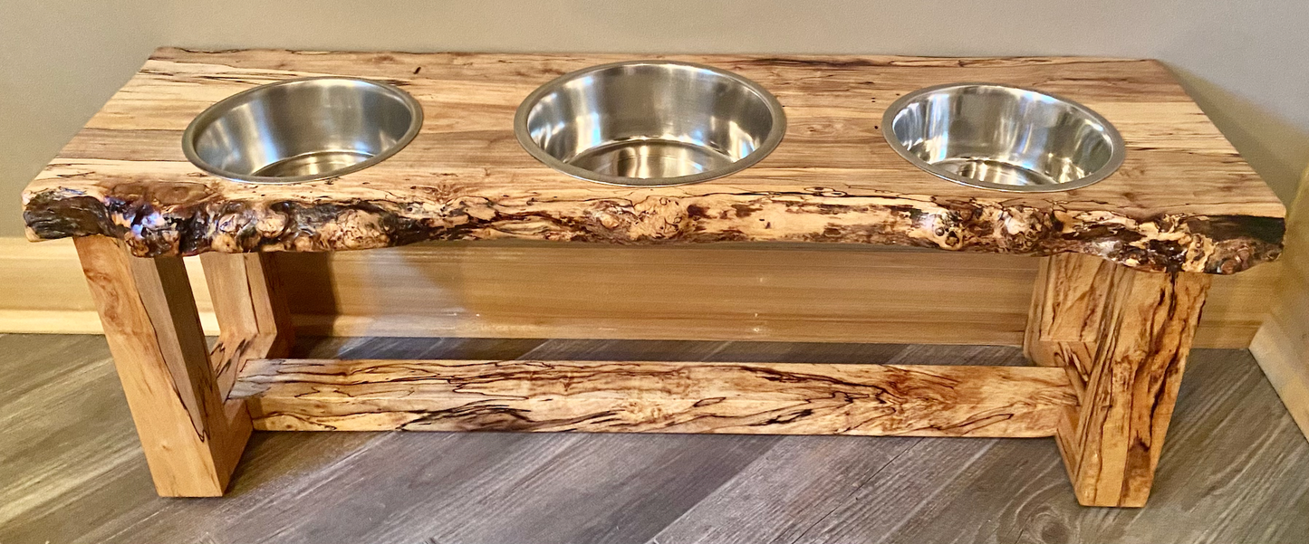 Live edge raised pet stand crafted from spalted maple or black walnut, featuring two stainless steel bowls for food and water. Elevated pet feeder, showcasing the natural wood grain and sturdy construction. Top-down view highlighting the placement of the three stainless steel bowls within the live edge wooden stand. Detailed close-up of the spalted maple’s unique wood grain patterns on the pet stand.