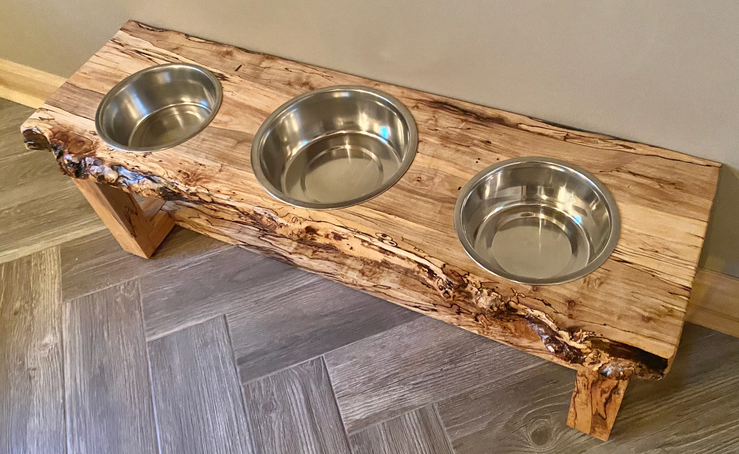 Live edge raised pet stand crafted from spalted maple or black walnut, featuring two stainless steel bowls for food and water. Elevated pet feeder, showcasing the natural wood grain and sturdy construction. Top-down view highlighting the placement of the three stainless steel bowls within the live edge wooden stand. Detailed close-up of the spalted maple’s unique wood grain patterns on the pet stand.