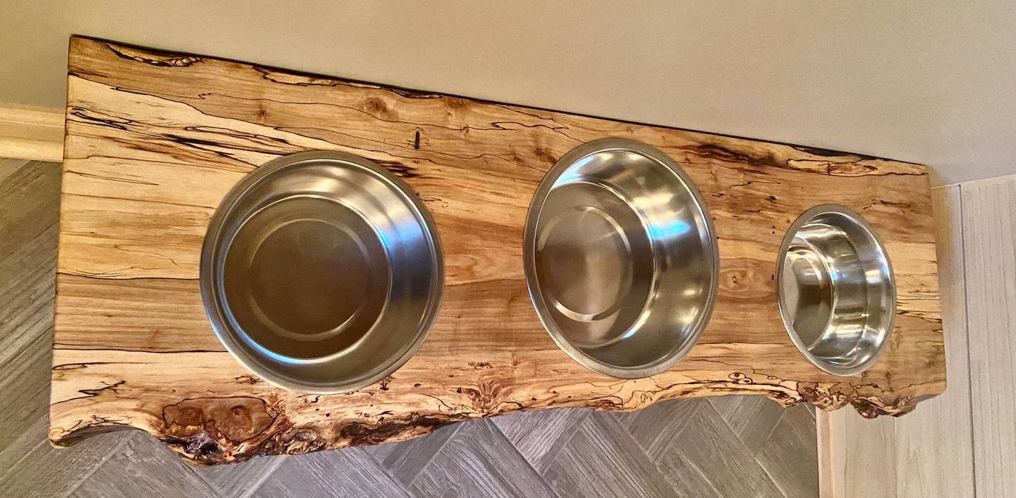 Live edge raised pet stand crafted from spalted maple or black walnut, featuring two stainless steel bowls for food and water. Elevated pet feeder, showcasing the natural wood grain and sturdy construction. Top-down view highlighting the placement of the three stainless steel bowls within the live edge wooden stand. Detailed close-up of the spalted maple’s unique wood grain patterns on the pet stand.