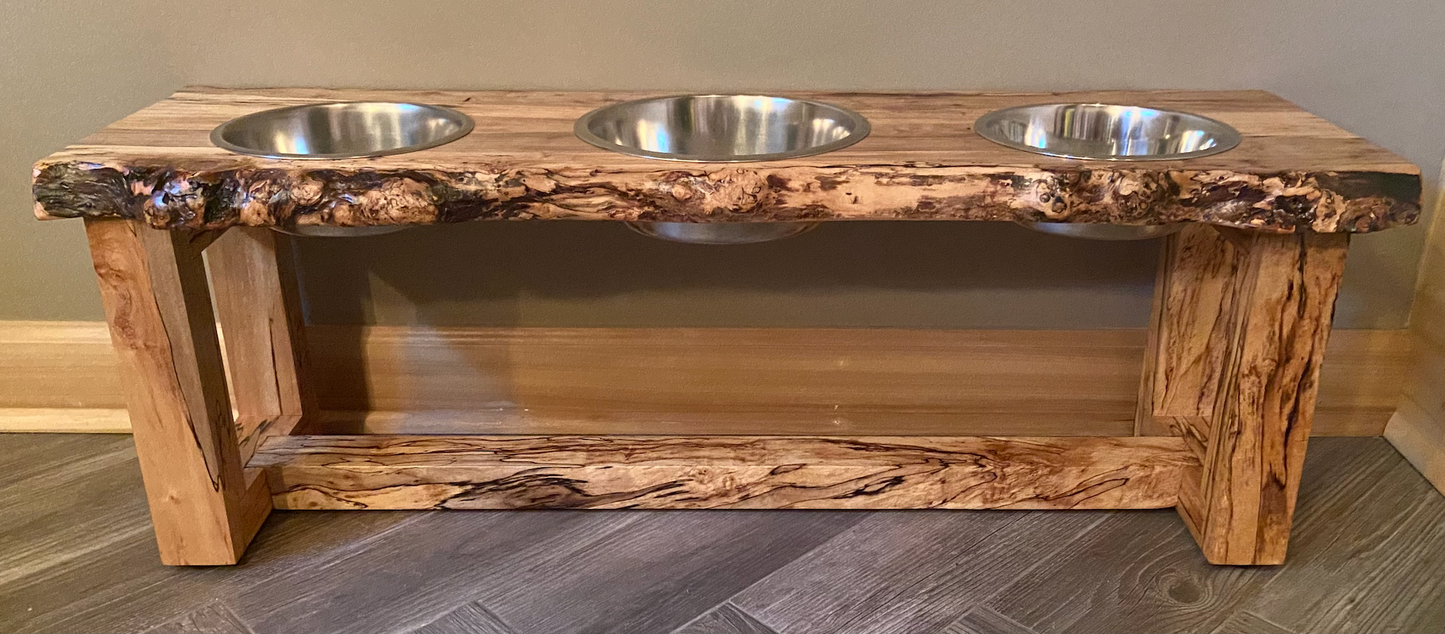 Live edge raised pet stand crafted from spalted maple or black walnut, featuring two stainless steel bowls for food and water. Elevated pet feeder, showcasing the natural wood grain and sturdy construction. Top-down view highlighting the placement of the three stainless steel bowls within the live edge wooden stand. Detailed close-up of the spalted maple’s unique wood grain patterns on the pet stand.