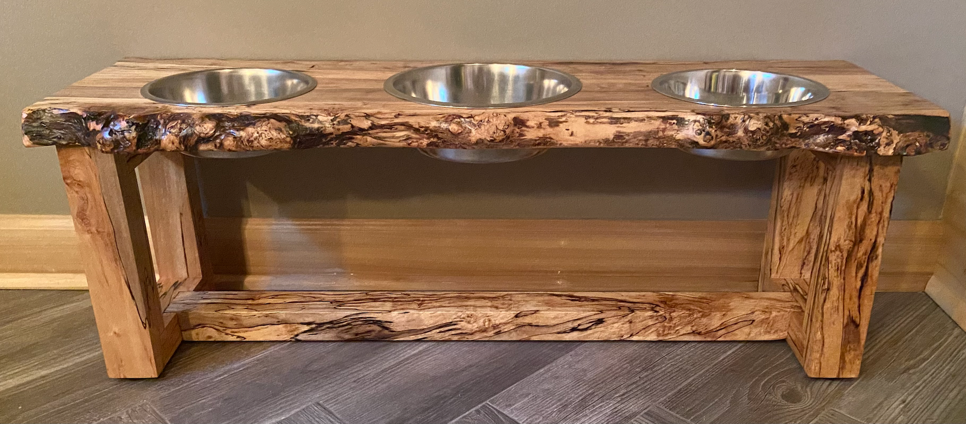 Live edge raised pet stand crafted from spalted maple or black walnut, featuring two stainless steel bowls for food and water. Elevated pet feeder, showcasing the natural wood grain and sturdy construction. Top-down view highlighting the placement of the three stainless steel bowls within the live edge wooden stand. Detailed close-up of the spalted maple’s unique wood grain patterns on the pet stand.