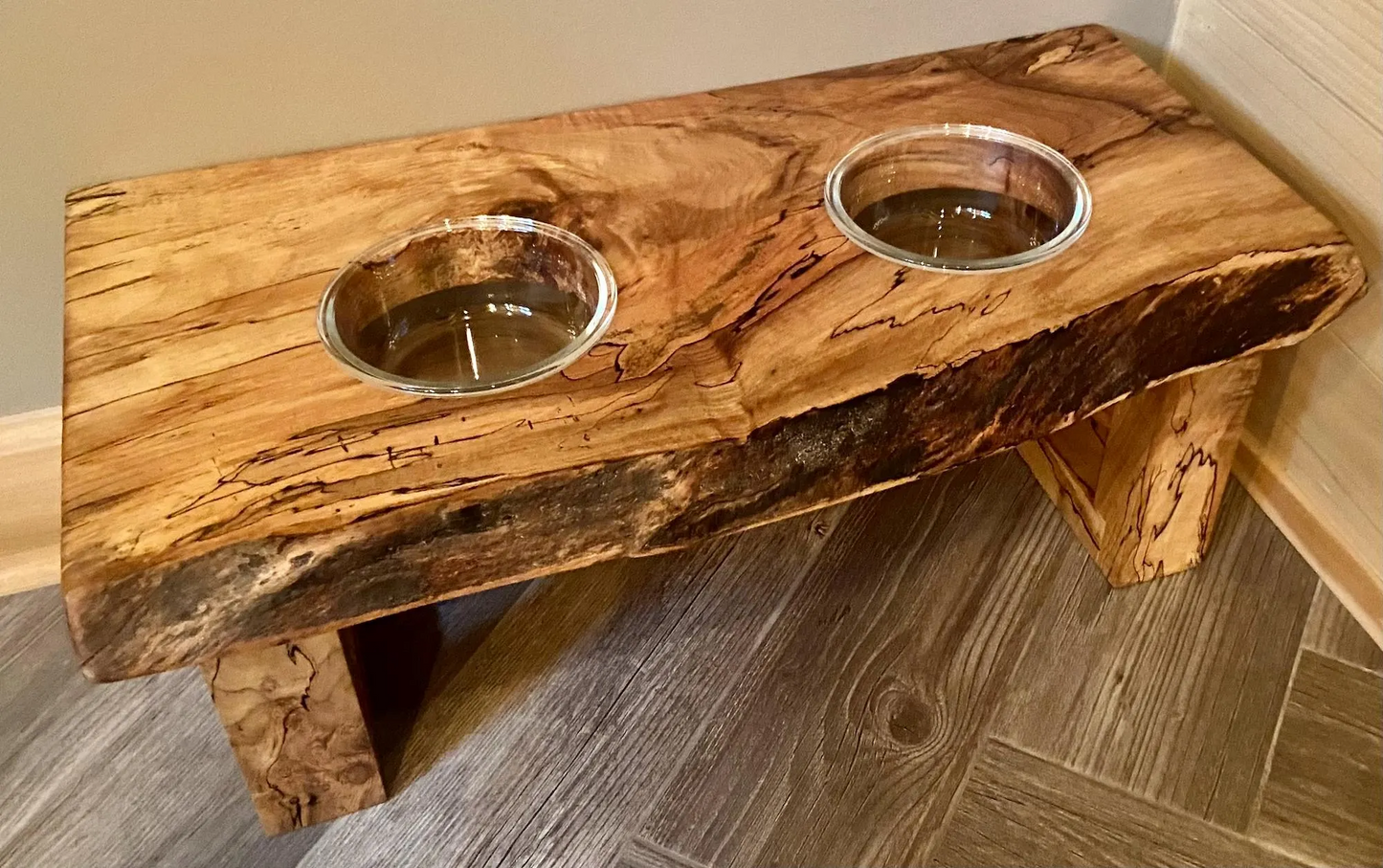 Live edge raised pet stand crafted from spalted maple or black walnut, featuring two stainless steel bowls for food and water. Elevated pet feeder, showcasing the natural wood grain and sturdy construction. Top-down view highlighting the placement of the three stainless glass bowls within the live edge wooden stand. Detailed close-up of the spalted maple’s unique wood grain patterns on the pet stand.