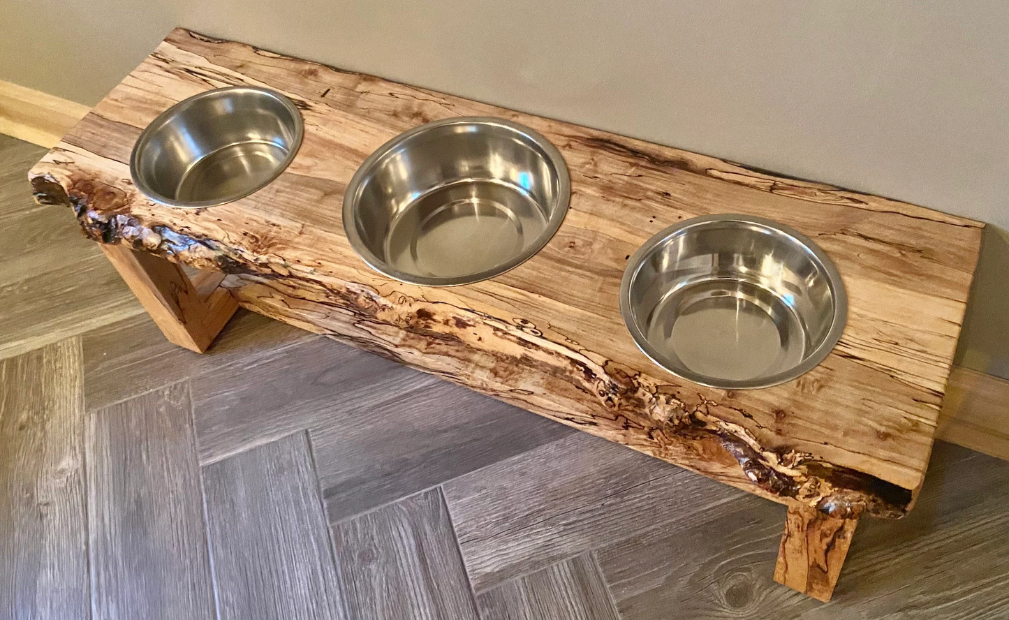 Live edge raised pet stand crafted from spalted maple or black walnut, featuring two stainless steel bowls for food and water. Elevated pet feeder, showcasing the natural wood grain and sturdy construction. Top-down view highlighting the placement of the three stainless steel bowls within the live edge wooden stand. Detailed close-up of the spalted maple’s unique wood grain patterns on the pet stand.