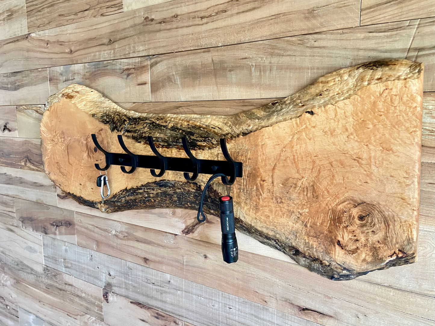 Live edge maple coat rack mounted on a wood-paneled wall, featuring 5 matte black metal hooks and natural wood grain patterns.