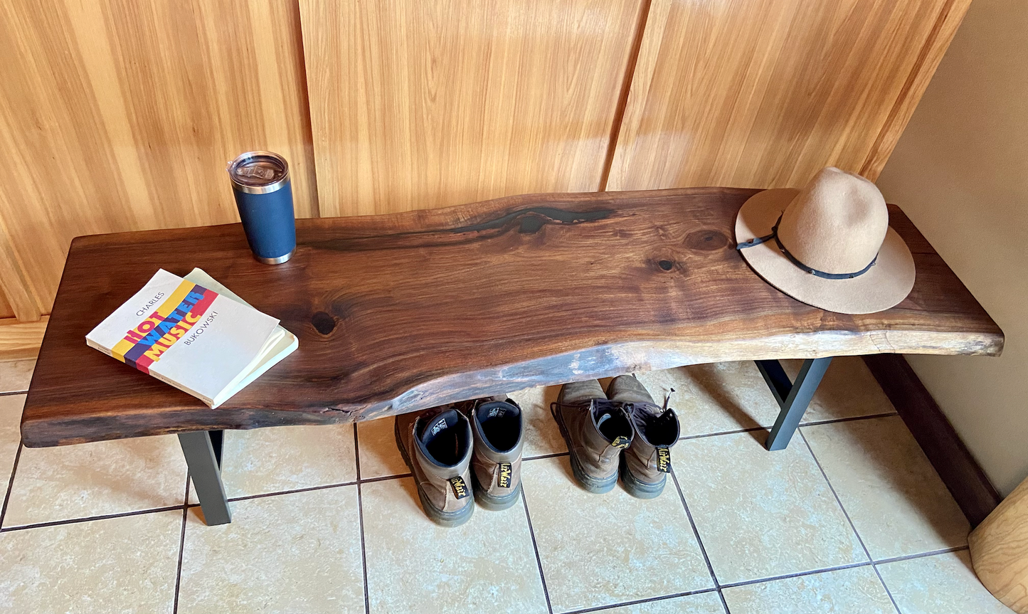 Live edge walnut bench with steel legs against a wood-paneled wall on tile flooring. Live edge walnut coffee table styled with everyday items, including boots underneath, showcasing its versatility and natural wood grain.