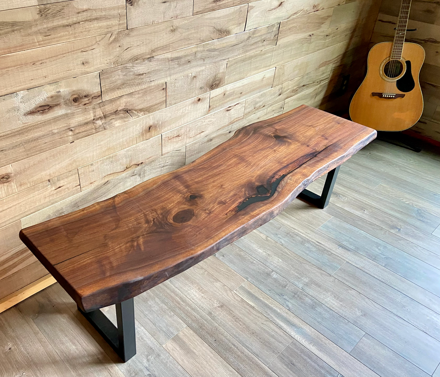 Live edge walnut bench with steel legs against a wood-paneled wall on wood flooring.