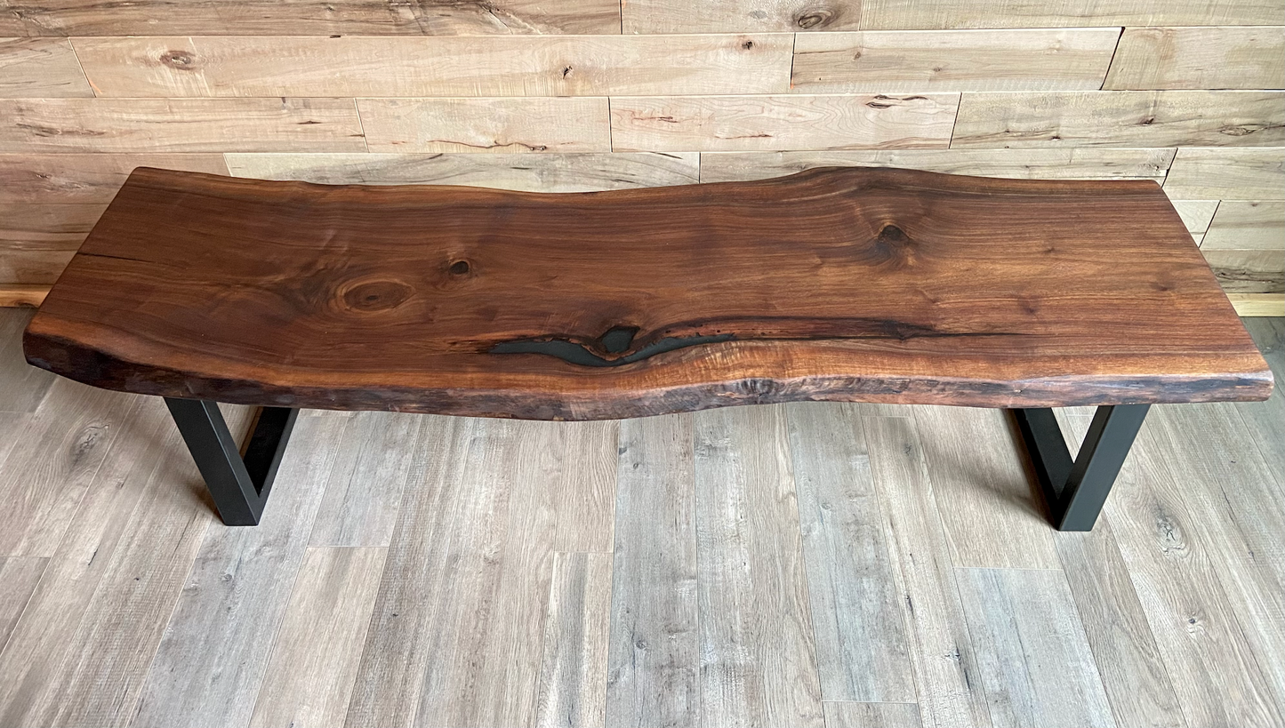 Live edge walnut bench with steel legs against a wood-paneled wall on wood flooring.