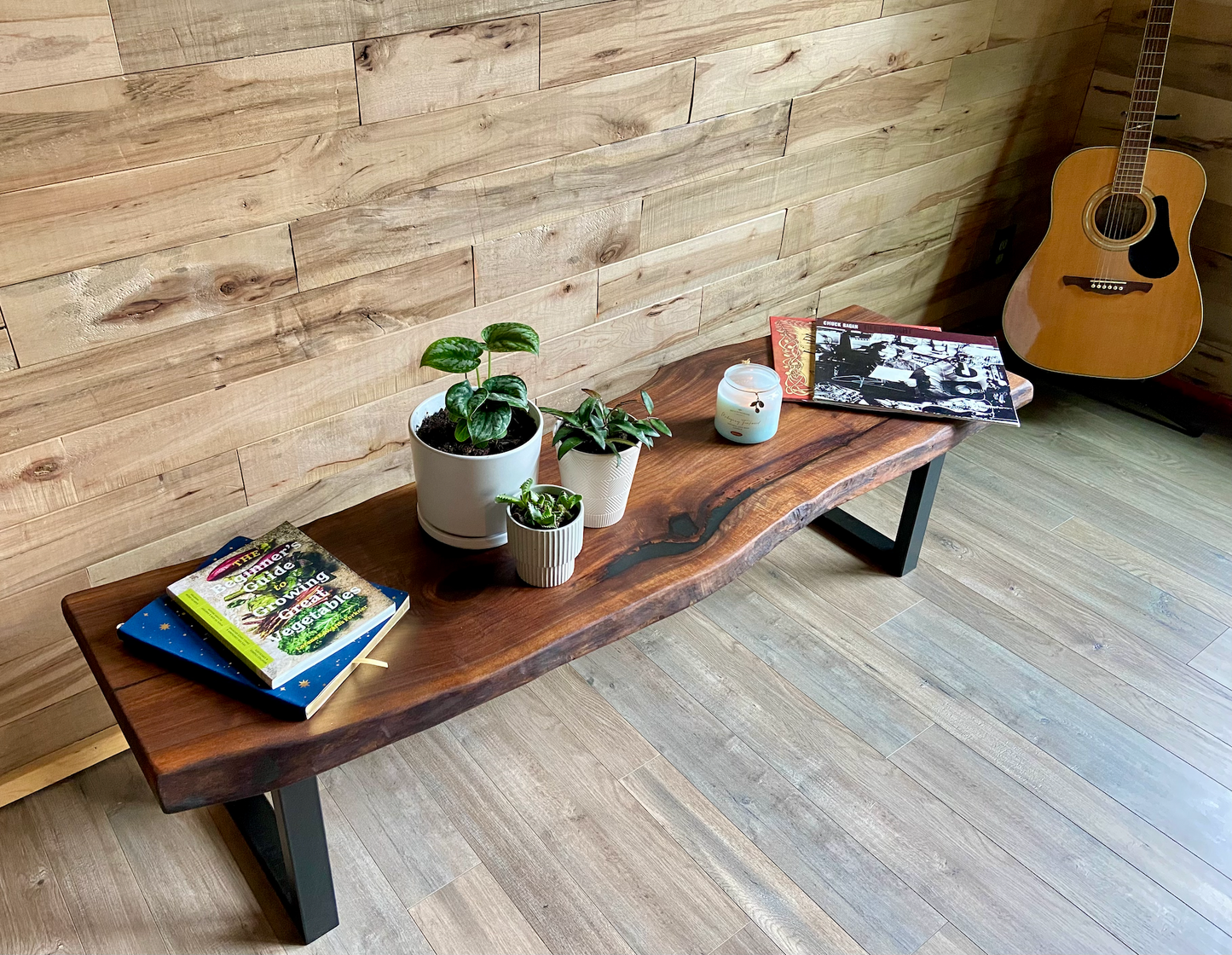 Live edge walnut bench with steel legs against a wood-paneled wall on wood flooring. Live edge walnut coffee table styled with everyday items, showcasing its versatility and natural wood grain.