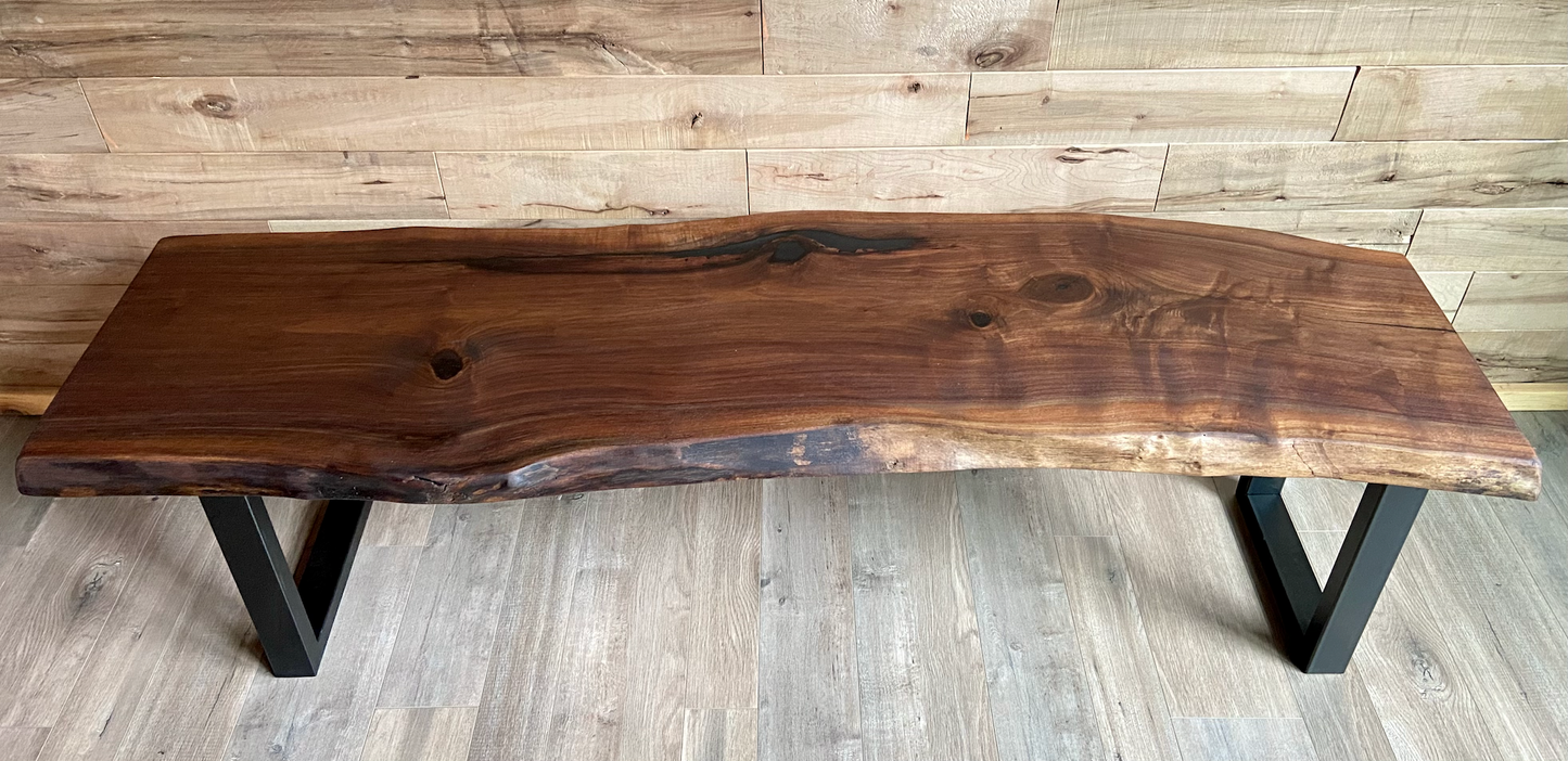 Live edge walnut bench with steel legs against a wood-paneled wall on wood flooring.