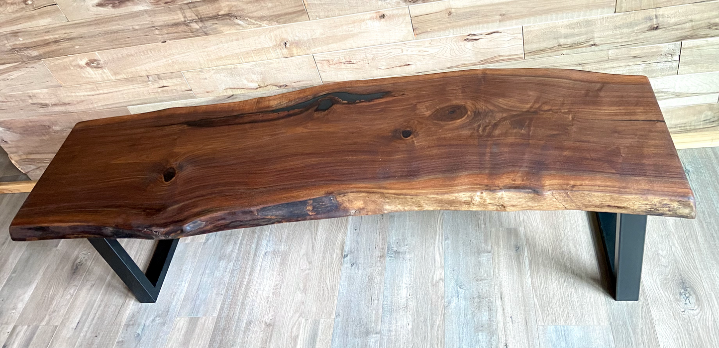 Live edge walnut bench with steel legs against a wood-paneled wall on wood flooring.