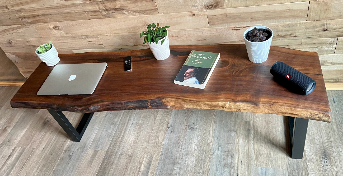 Live edge walnut bench with steel legs against a wood-paneled wall on wood flooring. Live edge walnut coffee table styled with everyday items, showcasing its versatility and natural wood grain.