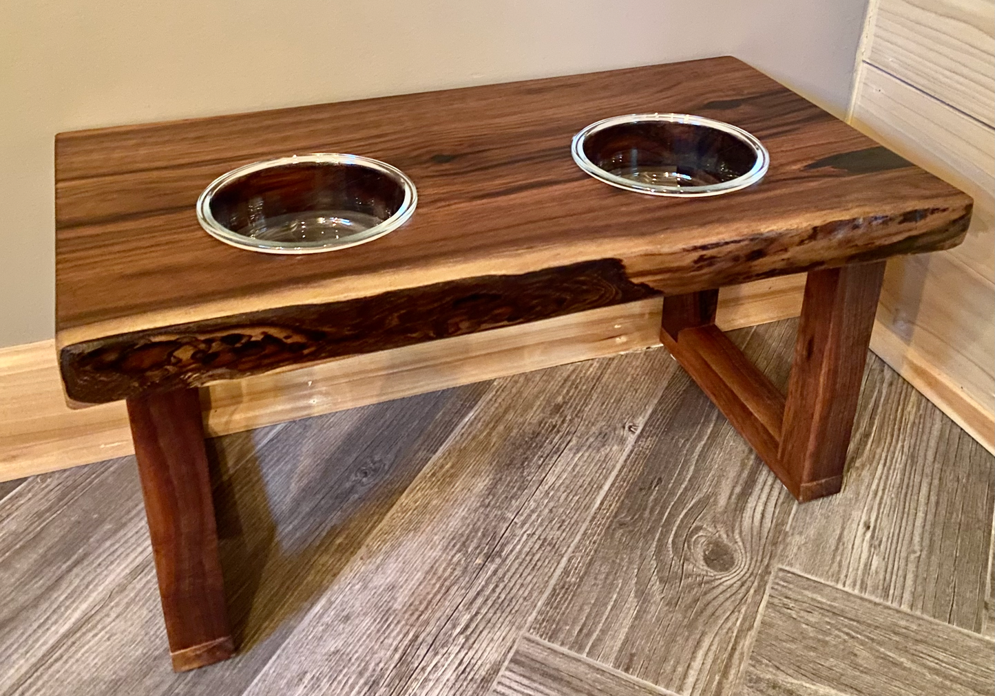 Live edge raised pet stand crafted from spalted maple or black walnut, featuring two stainless steel bowls for food and water. Elevated pet feeder, showcasing the natural wood grain and sturdy construction. Top-down view highlighting the placement of the two stainless glass bowls within the live edge wooden stand. Detailed close-up of the spalted maple’s unique wood grain patterns on the pet stand.