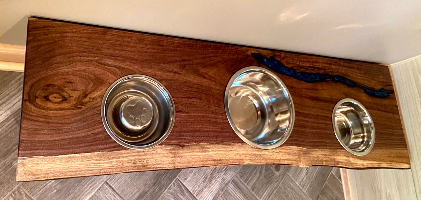 Live edge raised pet stand crafted from spalted maple or black walnut, featuring two stainless steel bowls for food and water. Elevated pet feeder, showcasing the natural wood grain and sturdy construction. Top-down view highlighting the placement of the three stainless steel bowls within the live edge wooden stand. Detailed close-up of the spalted maple’s unique wood grain patterns on the pet stand.