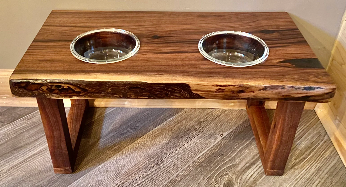 Live edge raised pet stand crafted from spalted maple or black walnut, featuring two stainless glass bowls for food and water. Elevated pet feeder, showcasing the natural wood grain and sturdy construction. Top-down view highlighting the placement of the two stainless steel bowls within the live edge wooden stand. Detailed close-up of the spalted maple’s unique wood grain patterns on the pet stand.