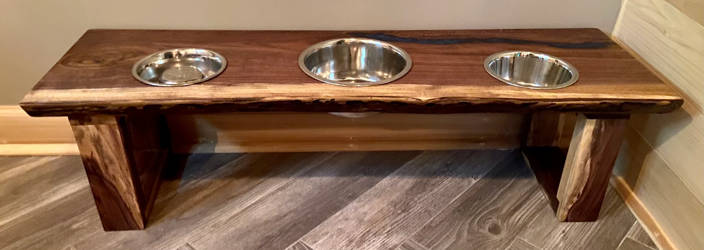 Live edge raised pet stand crafted from spalted maple or black walnut, featuring two stainless steel bowls for food and water. Elevated pet feeder, showcasing the natural wood grain and sturdy construction. Top-down view highlighting the placement of the three stainless steel bowls within the live edge wooden stand. Detailed close-up of the spalted maple’s unique wood grain patterns on the pet stand.