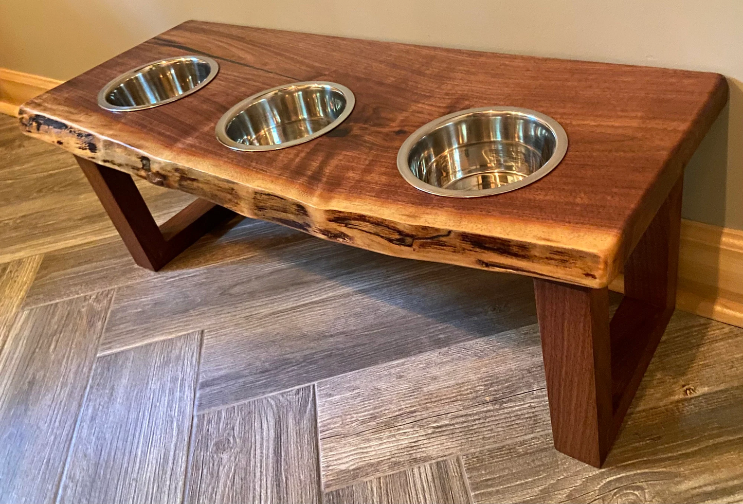 Live edge raised pet stand crafted from spalted maple or black walnut, featuring two stainless steel bowls for food and water. Elevated pet feeder, showcasing the natural wood grain and sturdy construction. Top-down view highlighting the placement of the three stainless steel bowls within the live edge wooden stand. Detailed close-up of the spalted maple’s unique wood grain patterns on the pet stand.