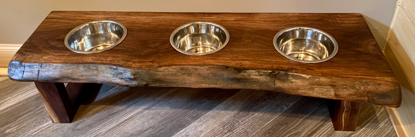 Live edge raised pet stand crafted from spalted maple or black walnut, featuring two stainless steel bowls for food and water. Elevated pet feeder, showcasing the natural wood grain and sturdy construction. Top-down view highlighting the placement of the three stainless steel bowls within the live edge wooden stand. Detailed close-up of the spalted maple’s unique wood grain patterns on the pet stand.