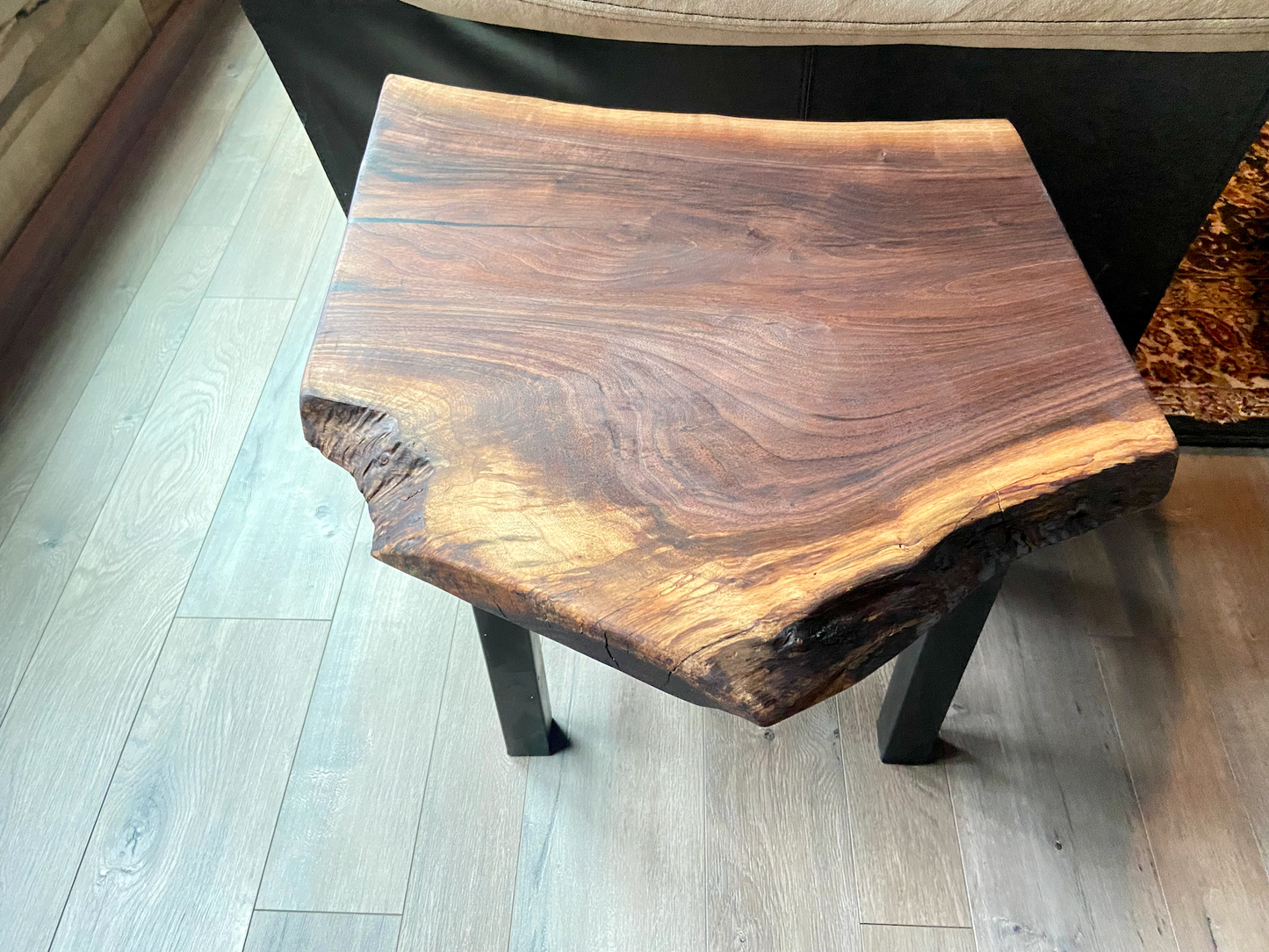 Top-down view of a live edge walnut side table with rich natural grain and smooth finish, set against a couch. Live edge walnut side table showing rustic charm and organic wood edge.