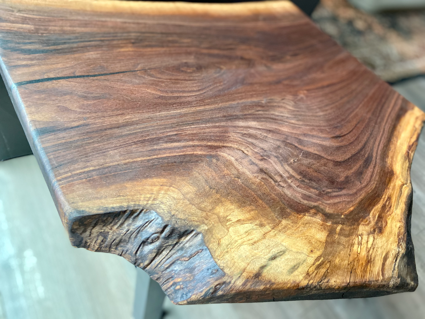 Top-down view of a live edge walnut side table with rich natural grain and smooth finish, set against a couch. Live edge walnut side table showing rustic charm and organic wood edge.