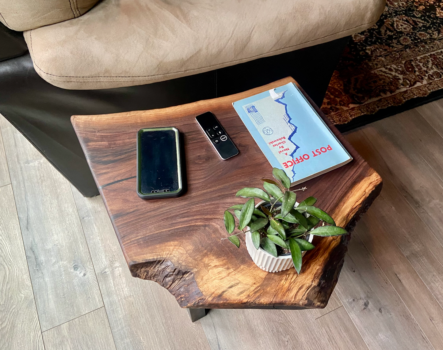Top-down view of a live edge walnut side table with rich natural grain and smooth finish, set against a couch. Live edge walnut side table styled with everyday items, showing rustic charm and organic wood edge.