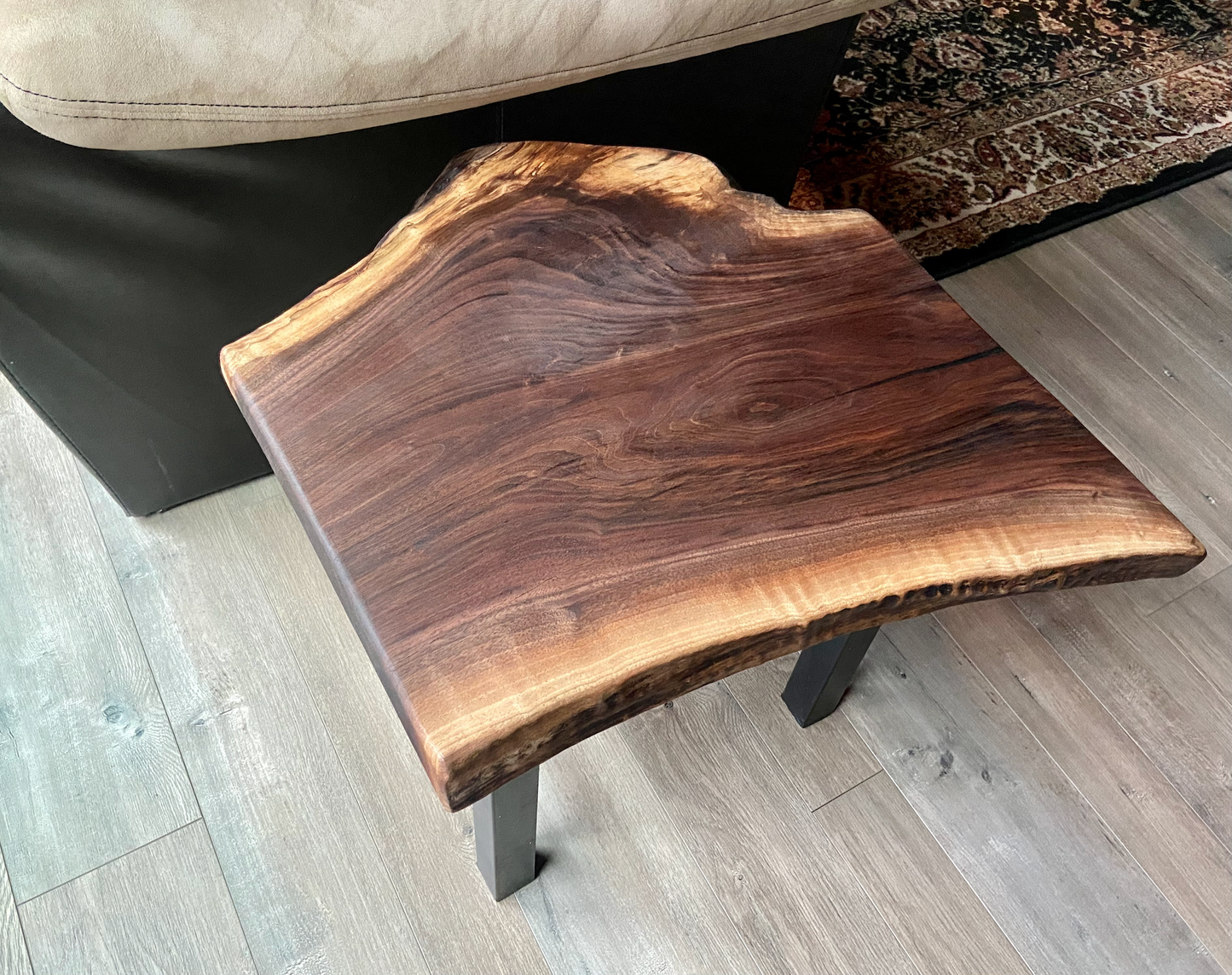 Top-down view of a live edge walnut side table with rich natural grain and smooth finish, set against a couch. Live edge walnut side table showing rustic charm and organic wood edge.