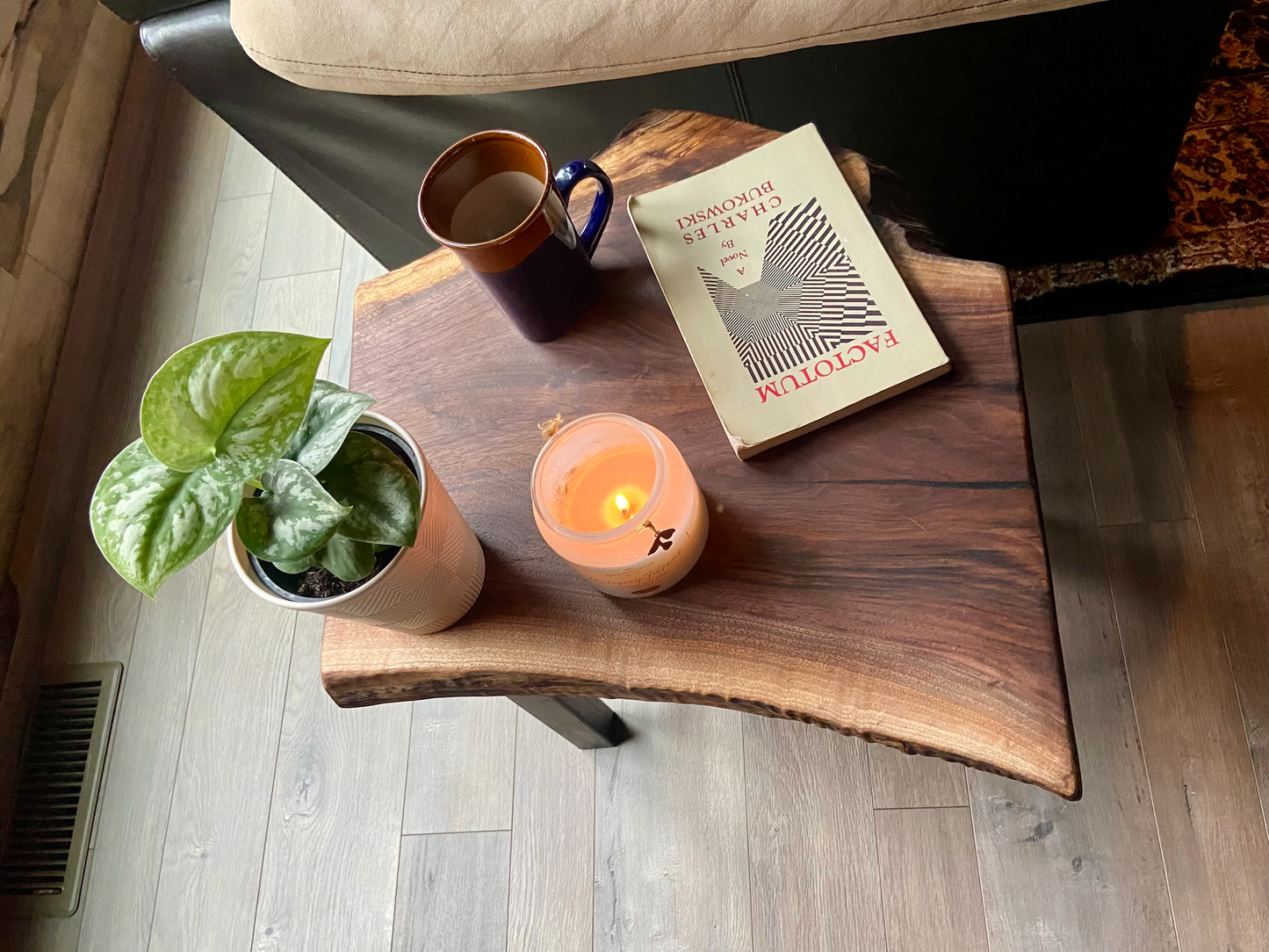 Top-down view of a live edge walnut side table with rich natural grain and smooth finish, set against a couch. Live edge walnut side table styled with everyday items, showing rustic charm and organic wood edge.