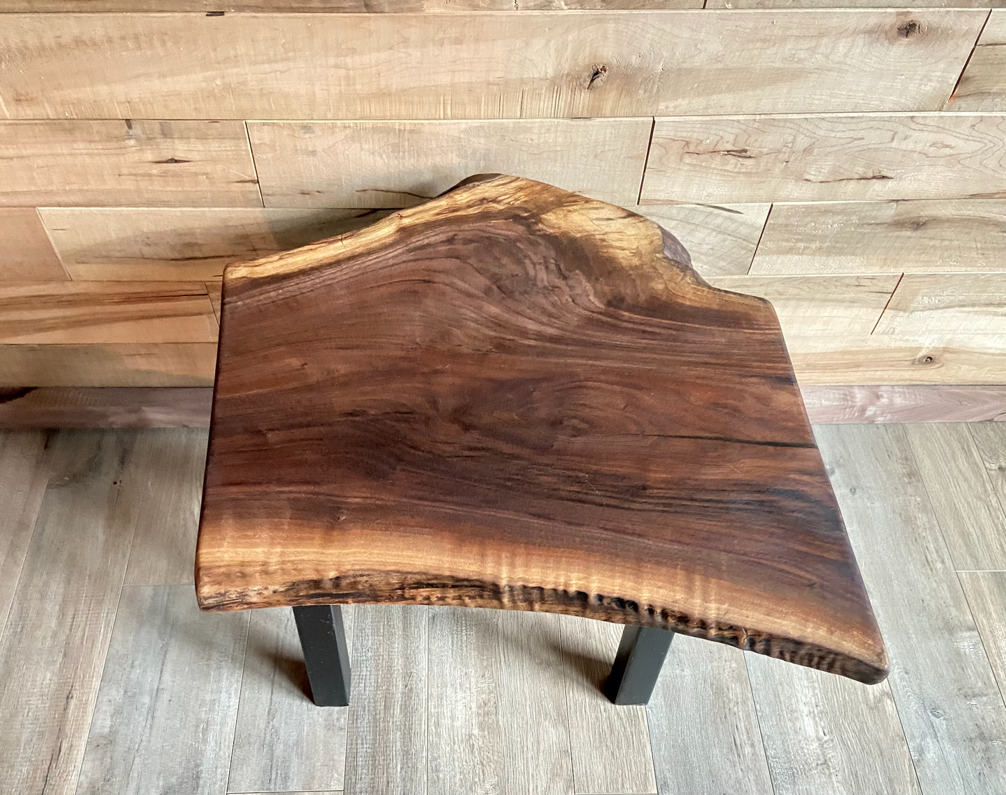 Top-down view of a live edge walnut side table with rich natural grain and smooth finish, set against a maple wall. Live edge walnut side table showing rustic charm and organic wood edge.