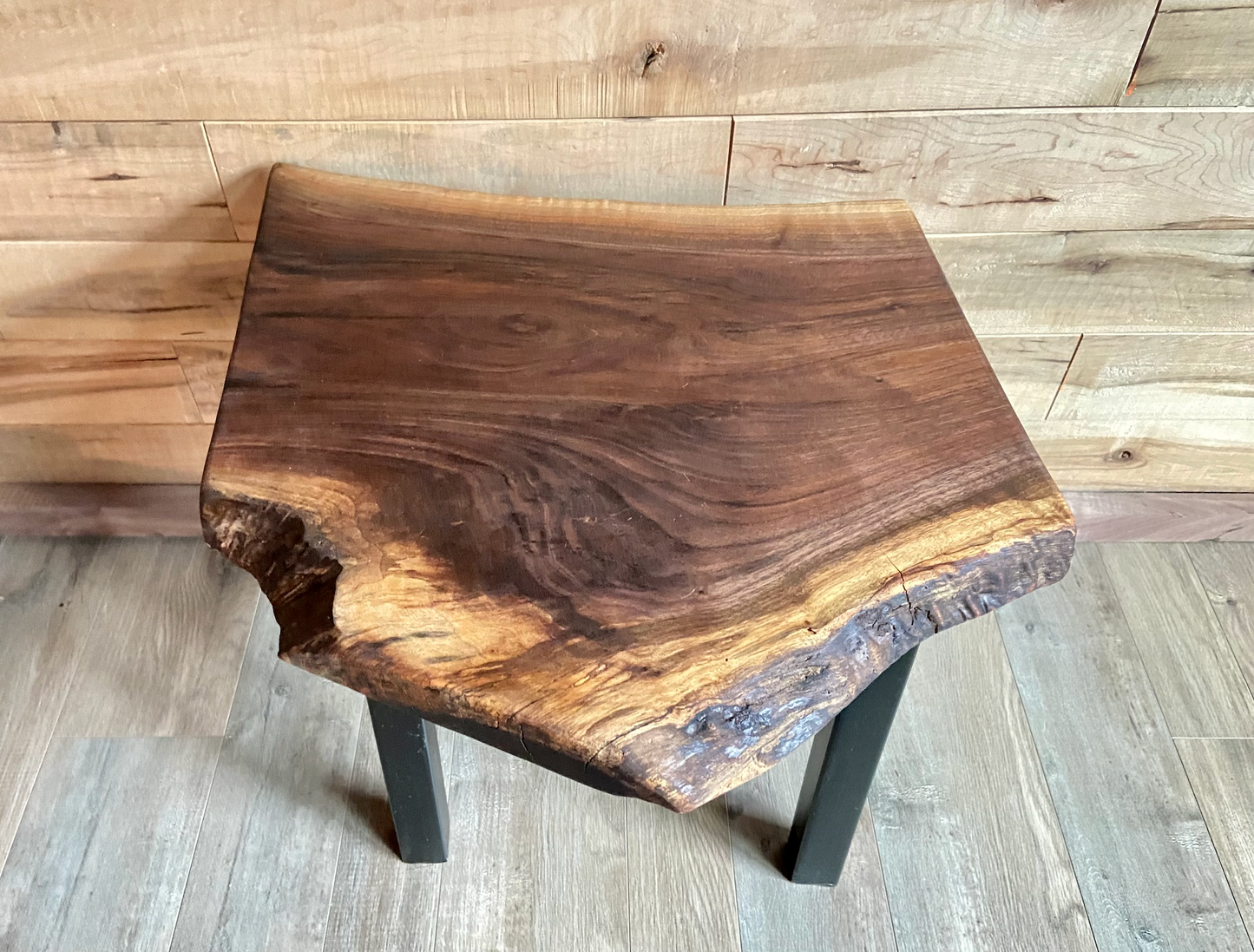 Top-down view of a live edge walnut side table with rich natural grain and smooth finish, set against a maple wall. Live edge walnut side table showing rustic charm and organic wood edge.