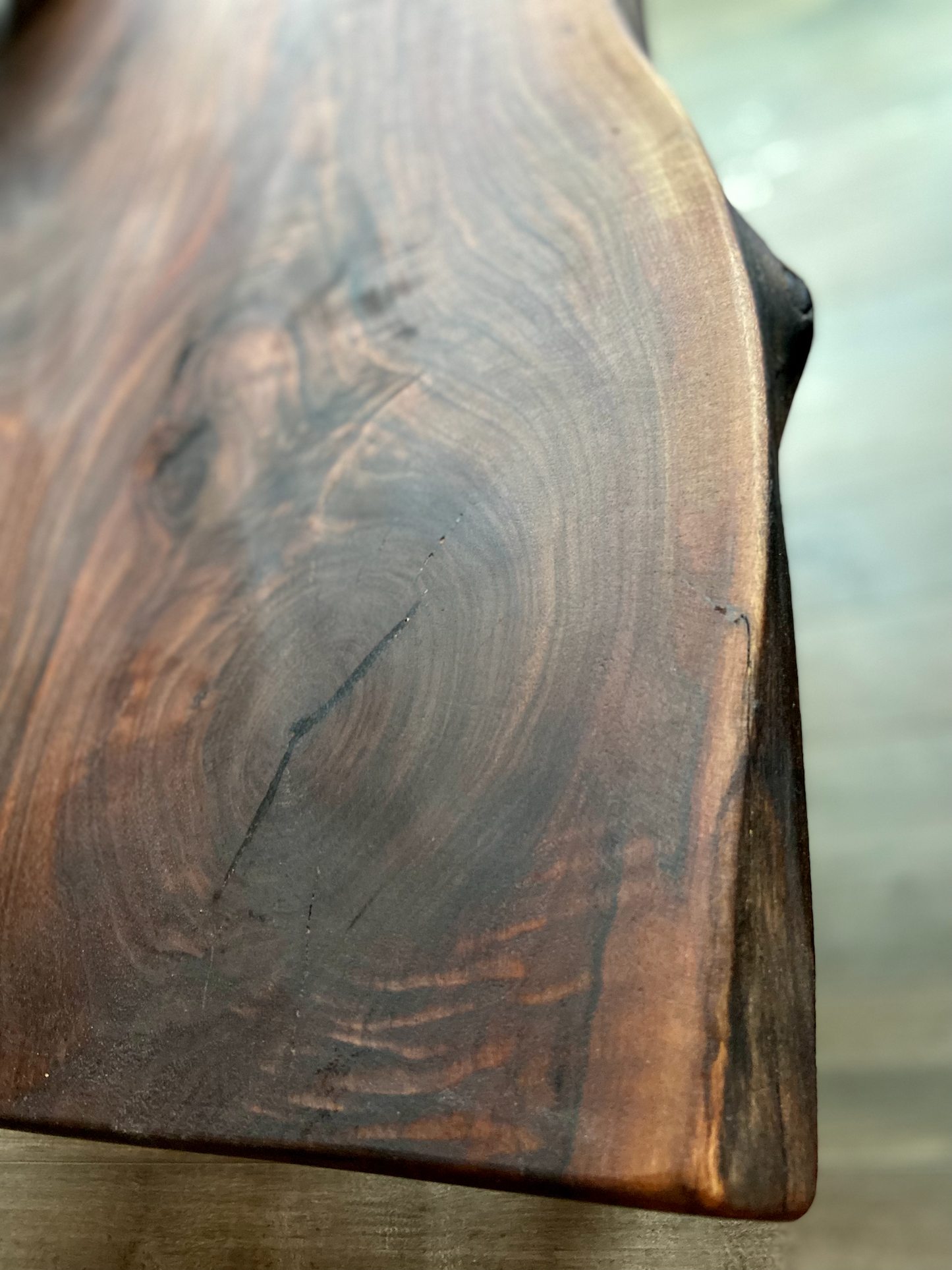 A handcrafted live edge walnut display table with black metal legs, placed against a couch. The live edge accent table showcases natural wood grain, knots, and organic edges, adding a rustic-modern touch to the space. The solid wood surface has a rich, natural finish, making it a perfect accent piece for an entryway or living space.