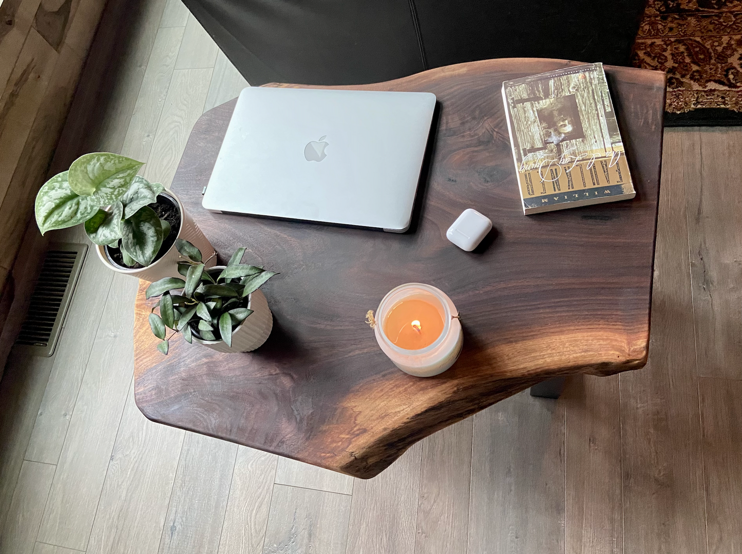 A handcrafted live edge walnut display table with black metal legs, placed against a couch. The live edge accenttable showcases natural wood grain, knots, and organic edges, adding a rustic-modern touch to the space. A live edge walnut bench styled with a candle, notebook, pen, a book, and a potted plant. The solid wood surface has a rich, natural finish, making it a perfect accent piece for an entryway or living space.