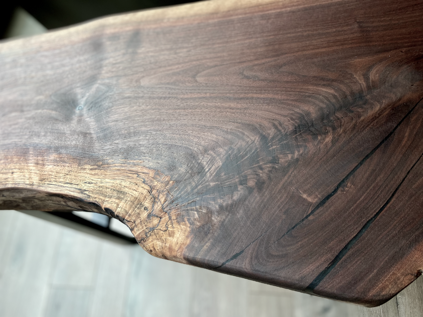 A handcrafted live edge walnut display table with black metal legs, placed against a couch. The live edge accenttable showcases natural wood grain, knots, and organic edges, adding a rustic-modern touch to the space. The solid wood surface has a rich, natural finish, making it a perfect accent piece for an entryway or living space.