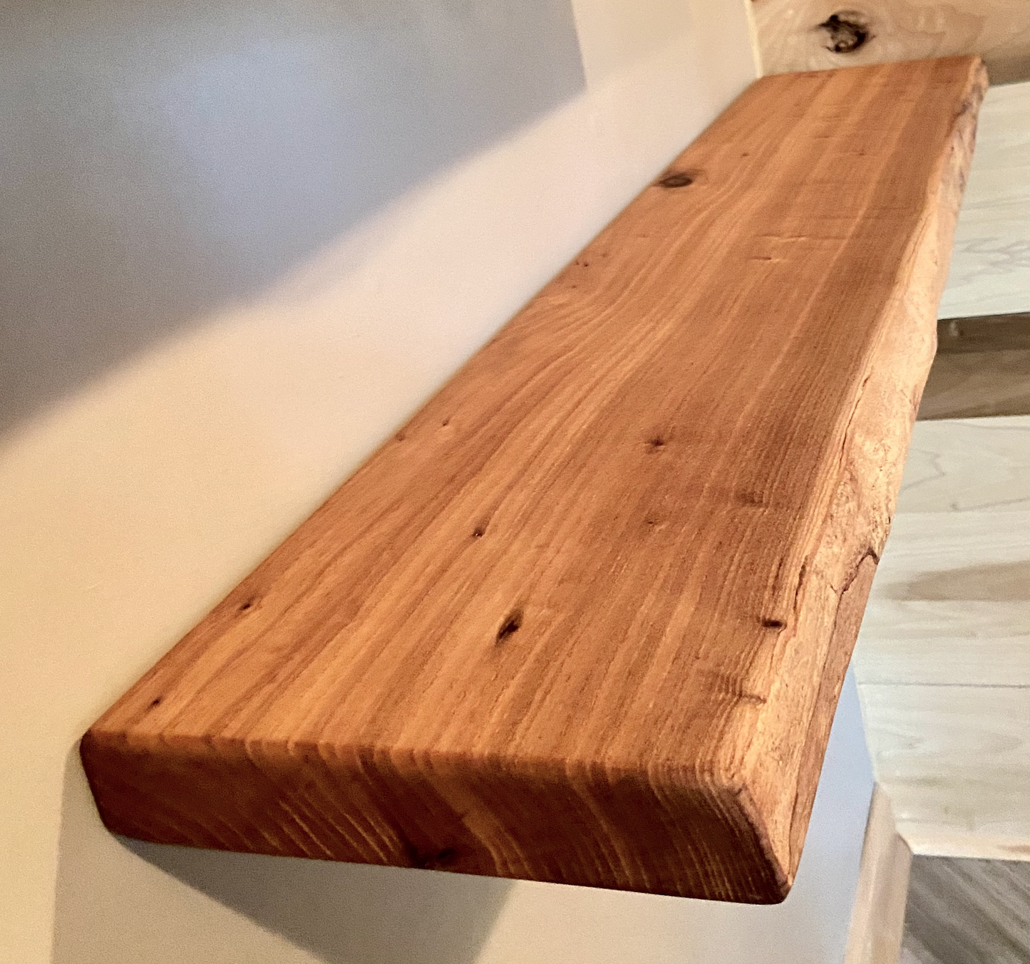 Close-up side view of a rustic live edge wood floating shelf showing natural grain and curvature.