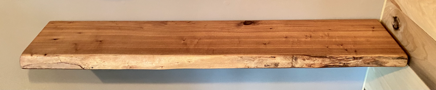 Close-up side view of a rustic live edge wood floating shelf showing natural grain and curvature.
