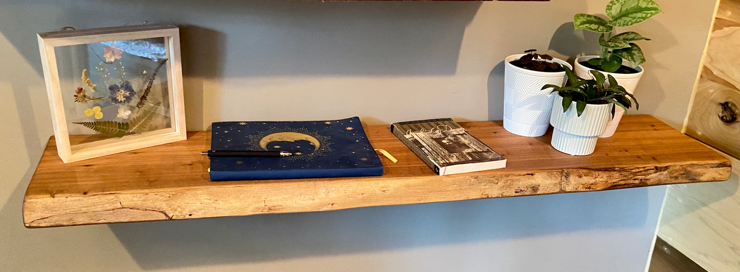Close-up side view of a rustic live edge wood floating shelf showing natural grain and curvature.