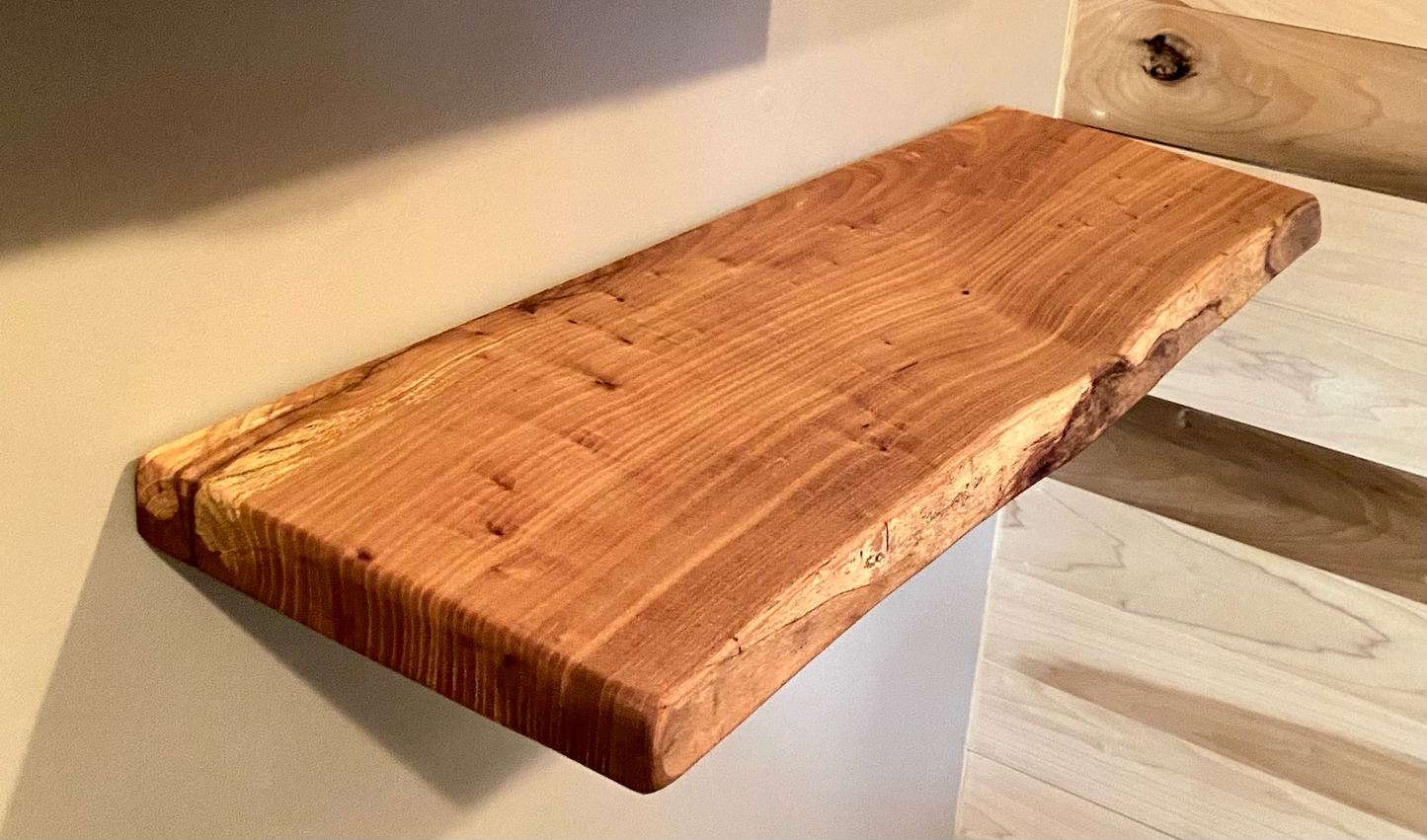 Close-up side view of a rustic live edge wood floating shelf showing natural grain and curvature.