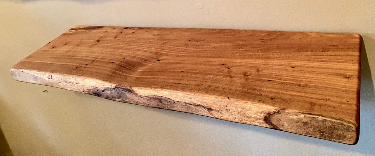 Close-up side view of a rustic live edge wood floating shelf showing natural grain and curvature.