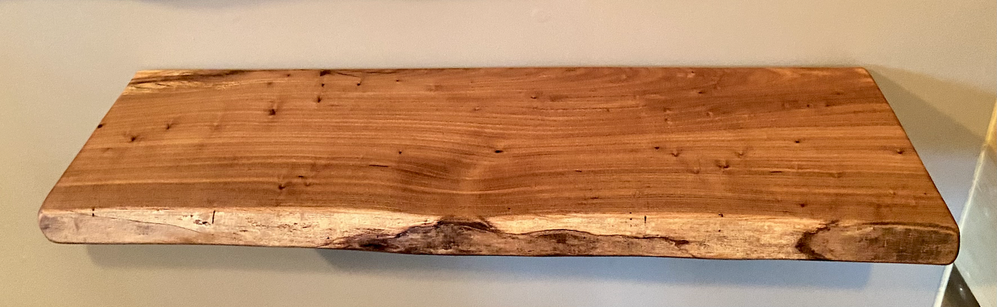 Close-up side view of a rustic live edge wood floating shelf showing natural grain and curvature.