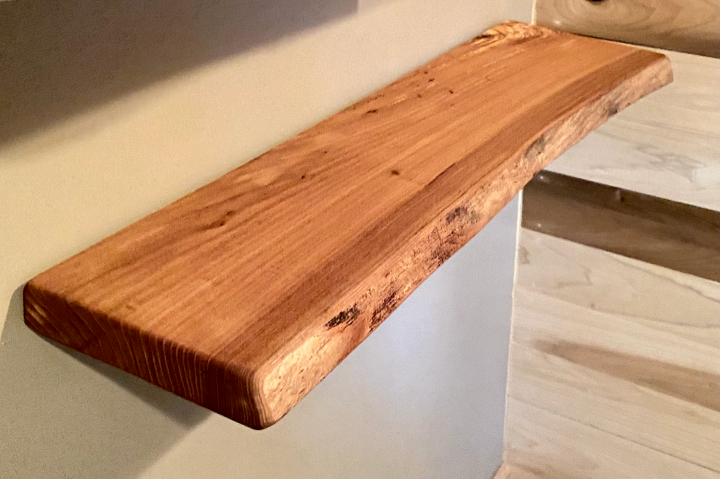 Close-up side view of a rustic live edge wood floating shelf showing natural grain and curvature.