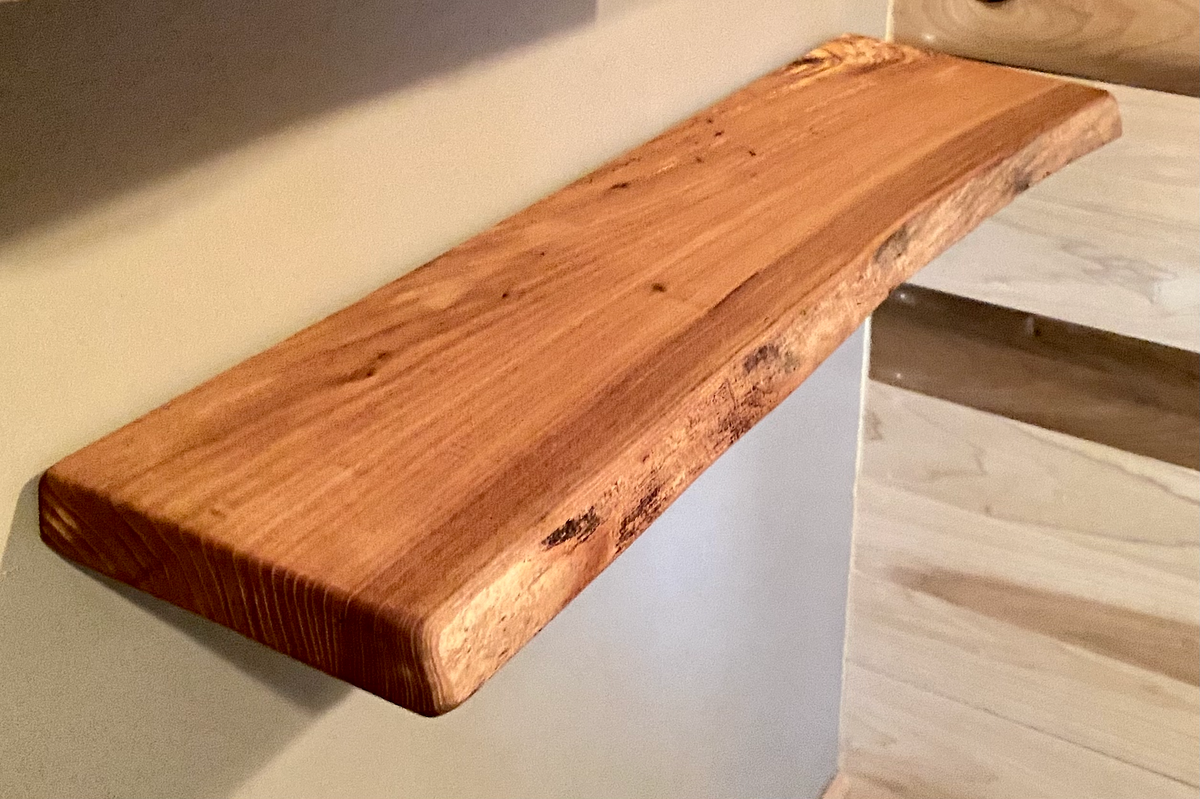 Close-up side view of a rustic live edge wood floating shelf showing natural grain and curvature.