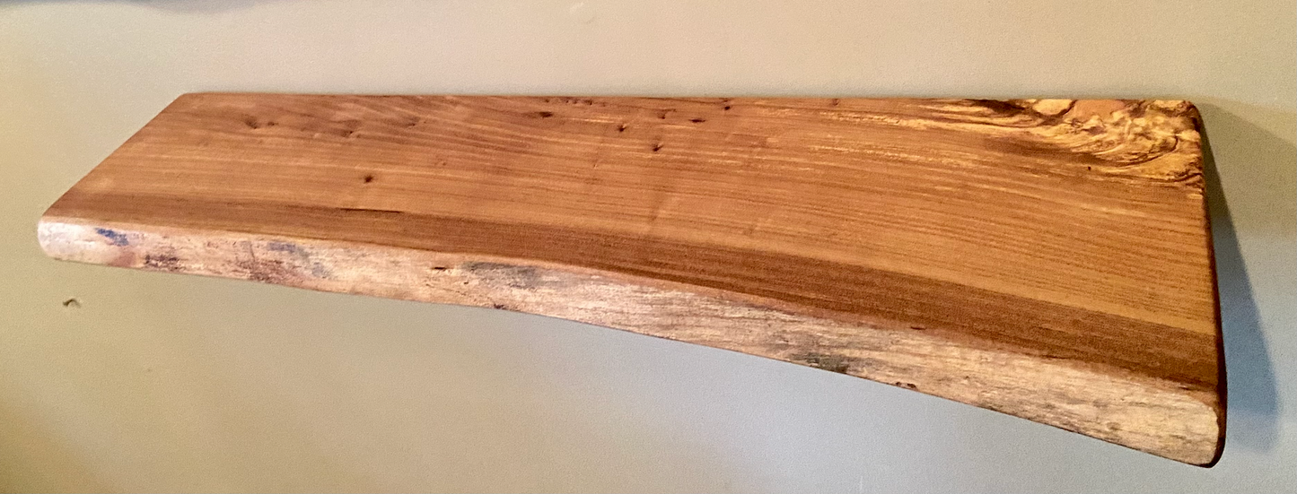 Close-up side view of a rustic live edge wood floating shelf showing natural grain and curvature.
