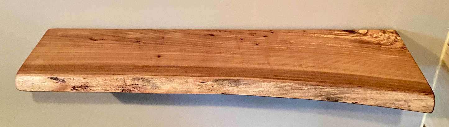 Close-up side view of a rustic live edge wood floating shelf showing natural grain and curvature.