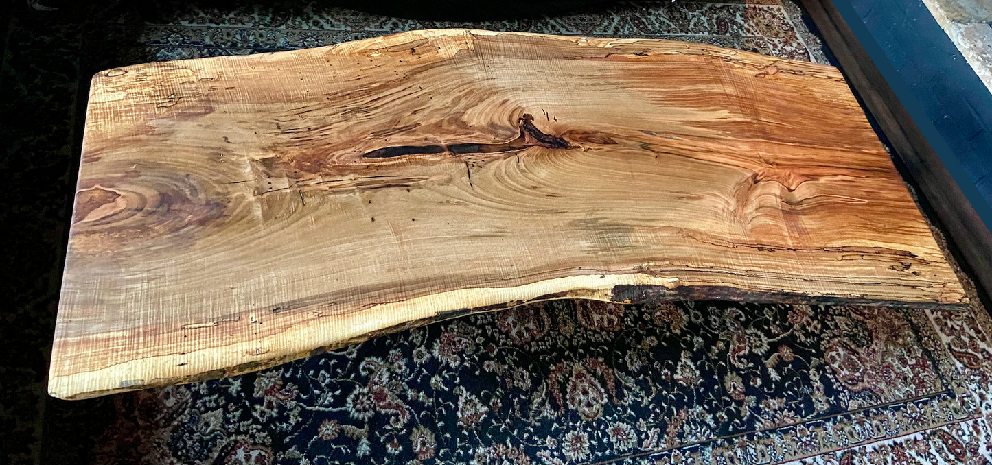 Top-down view of live edge ambrosia maple coffee table, highlighting natural wood grain, warm tones, and live edge details. Handcrafted ambrosia maple coffee table styled in a modern living room with a cozy, rustic aesthetic. Detailed view of ambrosia maple wood grain, showing natural spalting, color variations, and organic patterns. Curved live edge coffee table made from ambrosia maple, featuring unique grain patterns and a smooth, polished surface. Rustic and modern design.