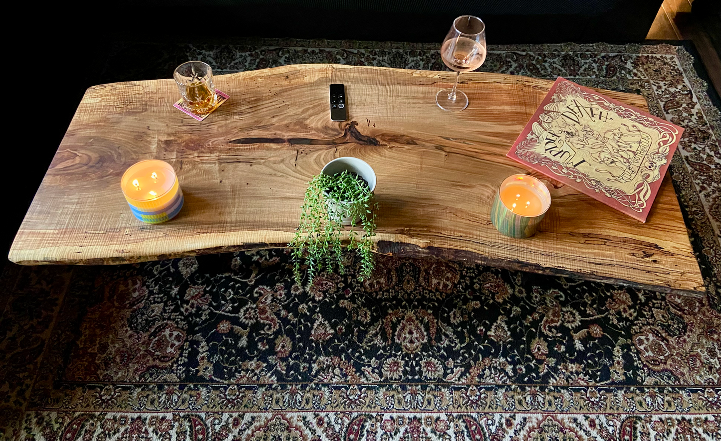 Top-down view of live edge ambrosia maple coffee table with household items, highlighting natural wood grain, and live edge details. Handcrafted ambrosia maple coffee table styled in a modern living room with a cozy, rustic aesthetic. Detailed view of ambrosia maple wood grain, showing natural spalting, color variations, and organic patterns. Curved live edge coffee table made from ambrosia maple, featuring unique grain patterns and a smooth, polished surface. Rustic and modern design.