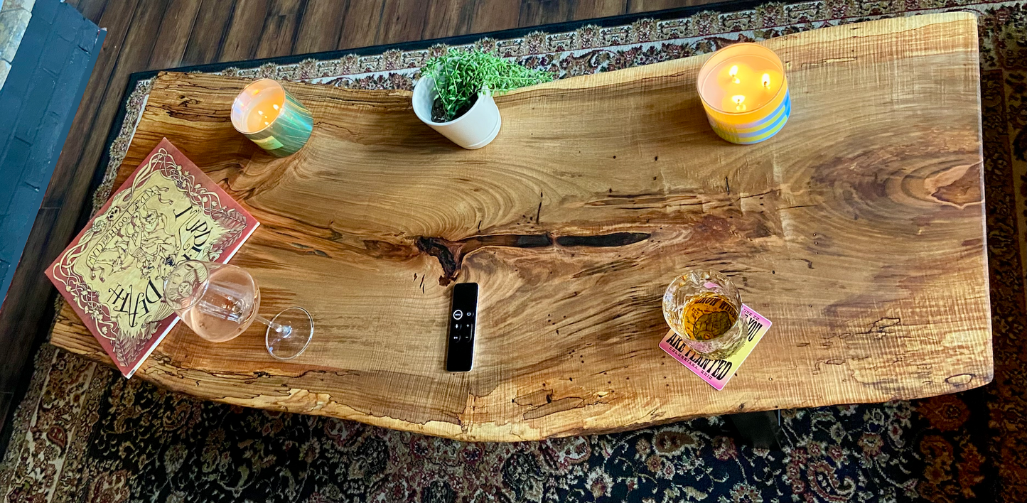 Top-down view of live edge ambrosia maple coffee table with household items, highlighting natural wood grain, and live edge details. Handcrafted ambrosia maple coffee table styled in a modern living room with a cozy, rustic aesthetic. Detailed view of ambrosia maple wood grain, showing natural spalting, color variations, and organic patterns. Curved live edge coffee table made from ambrosia maple, featuring unique grain patterns and a smooth, polished surface. Rustic and modern design.