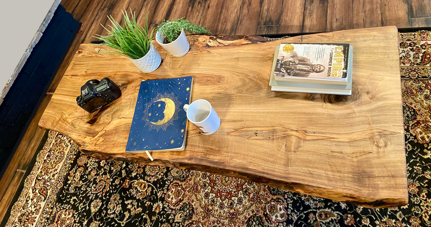 Top-down view of live edge ambrosia maple coffee table with household items, highlighting natural wood grain, and live edge details. Handcrafted ambrosia maple coffee table styled in a modern living room with a cozy, rustic aesthetic. Detailed view of ambrosia maple wood grain, showing natural spalting, color variations, and organic patterns. Curved live edge coffee table made from ambrosia maple, featuring unique grain patterns and a smooth, polished surface. Rustic and modern design.
